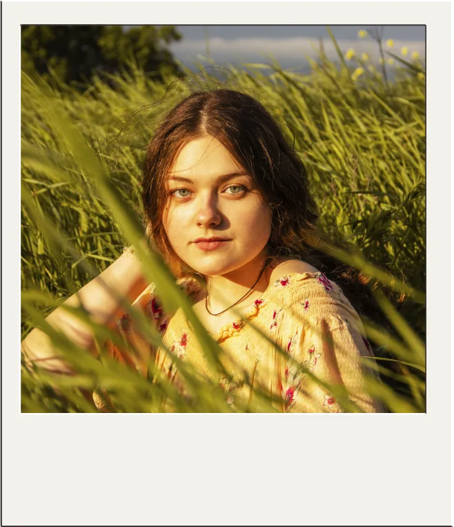 Polaroid photo of a woman sitting in a golden grass field.