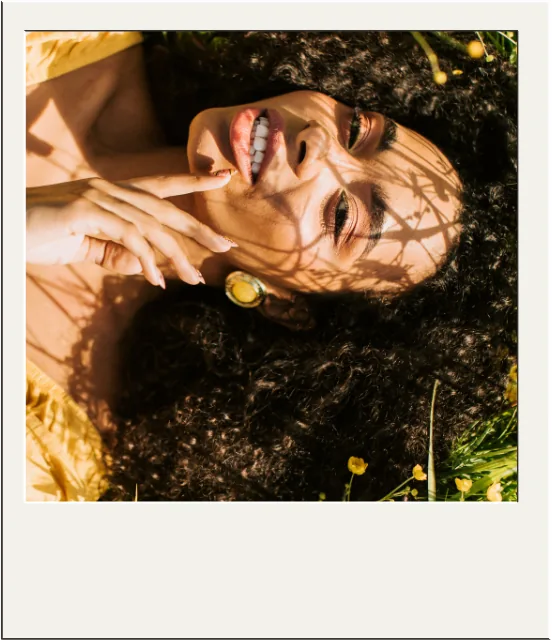 Polaroid photo of a woman lying in the grass, laughing in the sun.